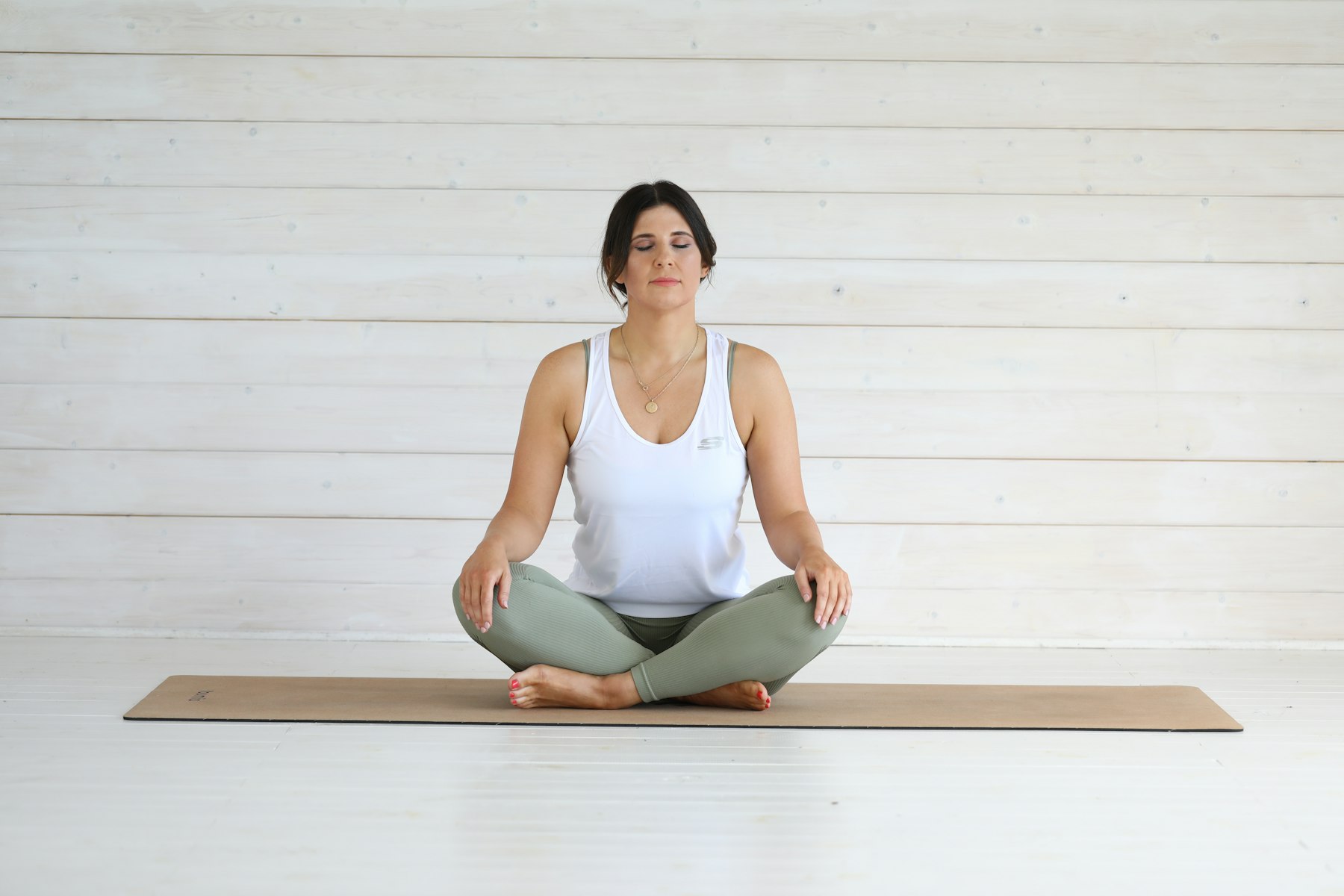 Frau sitzt ruhig und mit geschlossenen Augen auf einer Yogamatte — Pause statt Optimierung